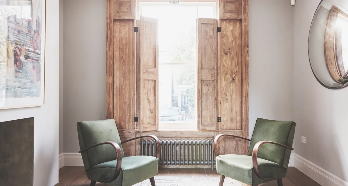 Two green armchairs beside a tall window with original wooden shutters