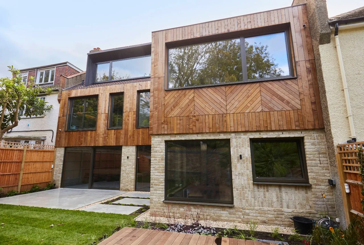Completed house extension with timber cladding, large dark-framed windows and a light brick ground floor.