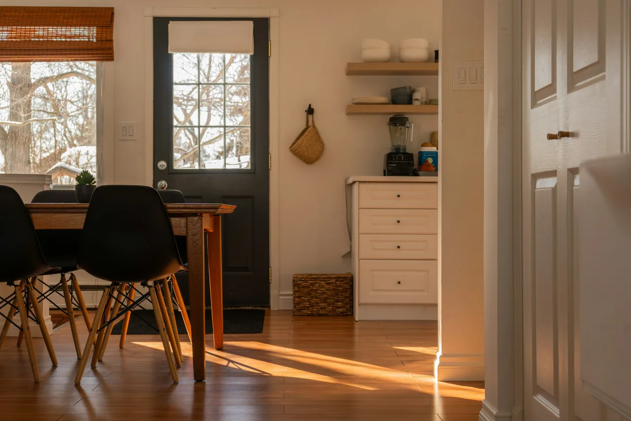 Stock illustration of a sunlit dining room with painted cabinetry, timber flooring and a garden door.